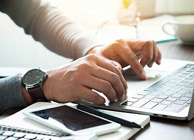 man taking notes while using a laptop