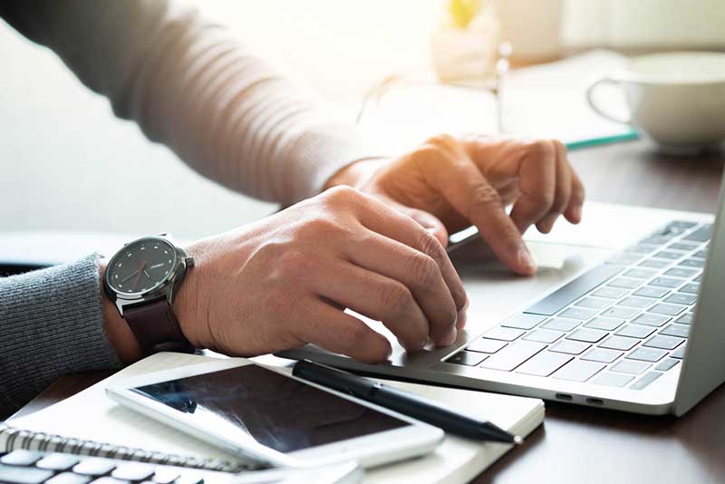 man taking notes while using a laptop